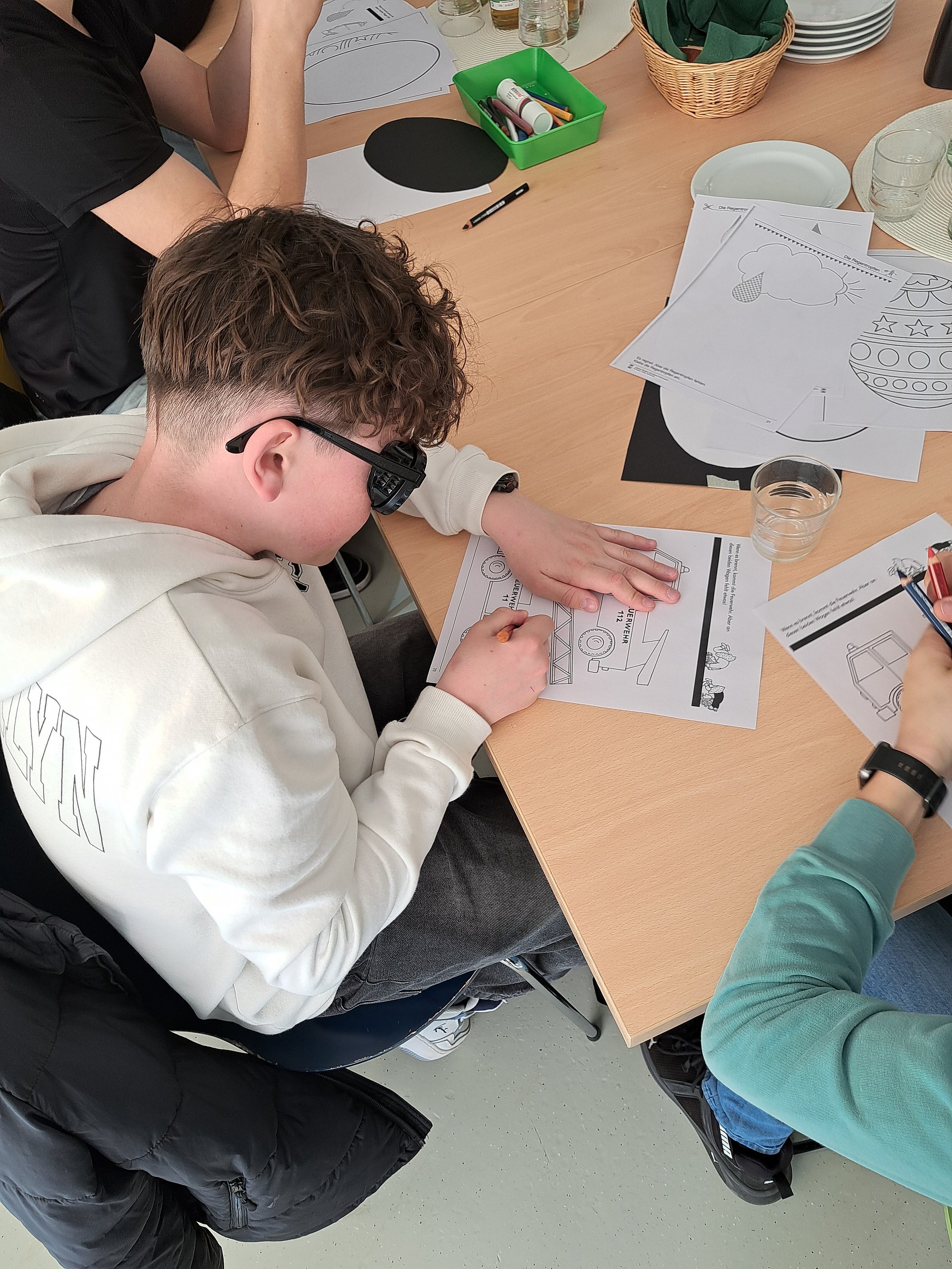 Ein Schüler sitzt an einem Tisch und liest ein Papierdokument. Er trägt eine Simulationsbrille