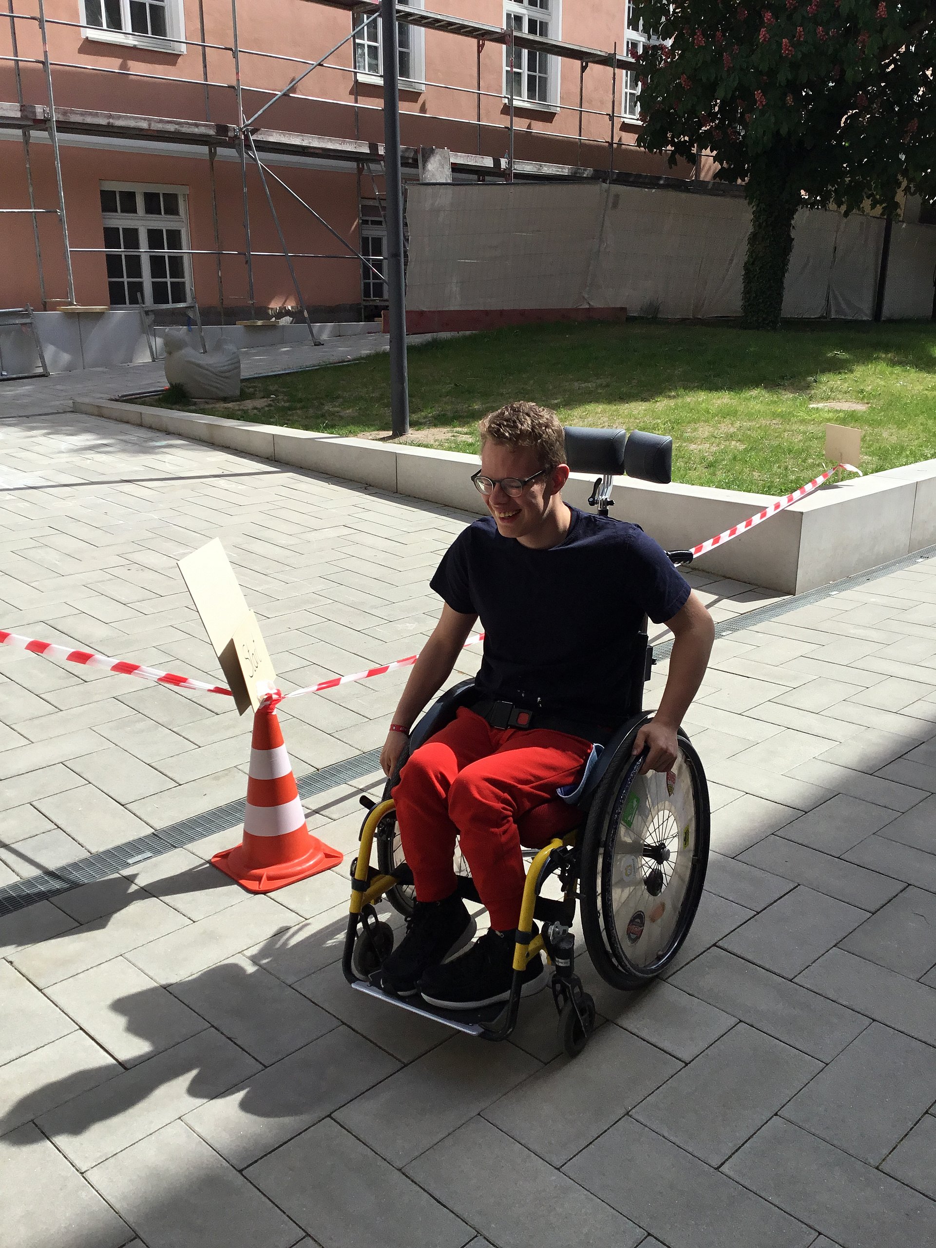 Ein Schüler trägt Sportkleidung und fährt mit einem Rollstuhl auf dem Schulgelände