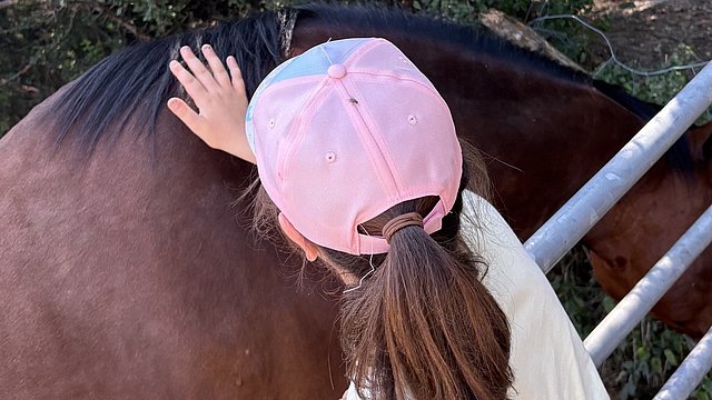 Ein Mädchen mit einer rosa Cappie streichelt den Rücken eines Pferdes