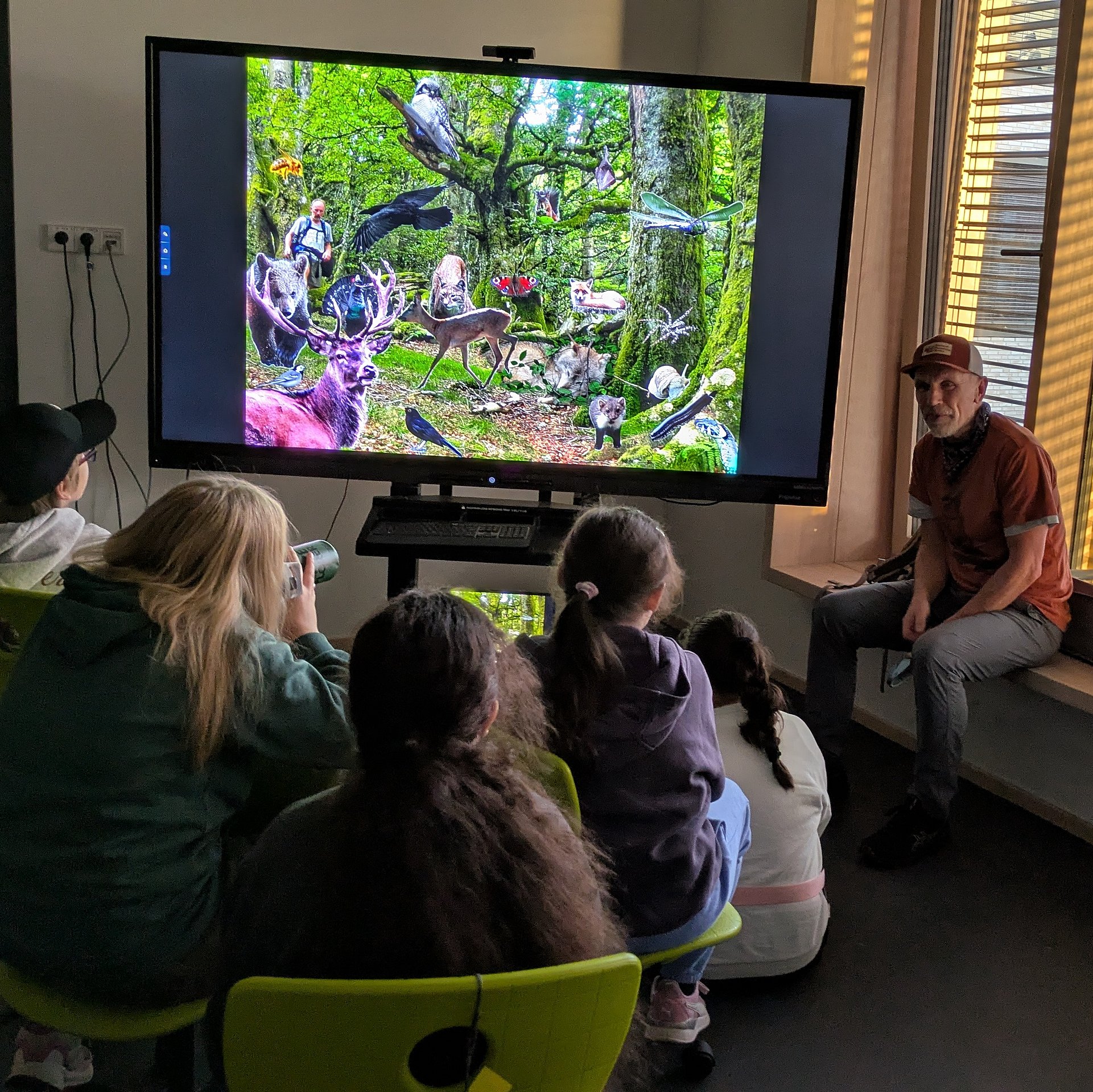 Schülerinnen und Schüler sitzen im Klassenzimmer vor einem großen Bildschirm und sehen sich einen Film an. 